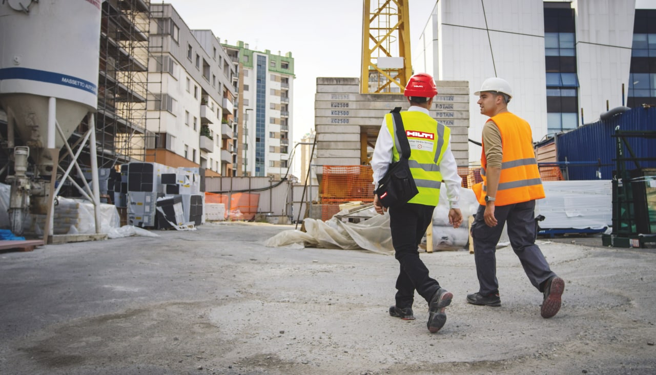 Zaměstnanec Hilti a stavebník jdou směrem ke stavbě s jeřábem